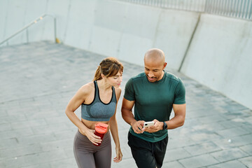 Smiling active young couple jogging exercising and having fun and laughing together taking a breakand using a mobile phone after walking and running in the park, fitness and healhty living concept