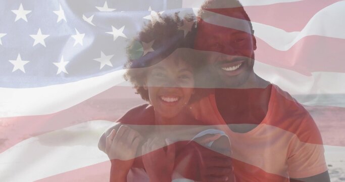 Hugging couple standing on sandy shoreline, under translucent American flag overlay - Powered by Adobe