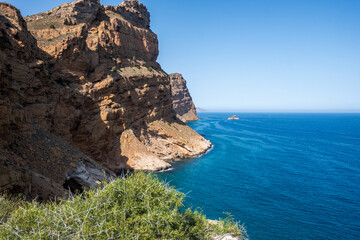Spain, Benidorm, coastal cliffs rise dramatically above the tranquil blue Mediterranean Sea, showcasing rugged rocks and vibrant greenery, perfect for vacation inspiration and nature exploration