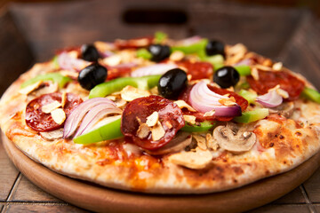 Pizza with chorizo ​​sausage, mozzarella cheese, green pepper and black olives. Rustic wooden background. Soft focus.	