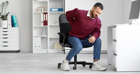 Young man suffering from back pain at table in office