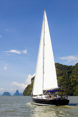 Sailboat sailing through Phang Nga Bay near Phuket, Thailand on a sunny day.