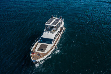 Modern white passenger boat with solar panels cruising through deep blue sea waters, aerial drone view of luxury yacht creating wake, maritime travel