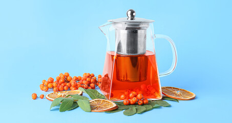 Teapot with tasty rowan tea, berries and dried orange slices on color background