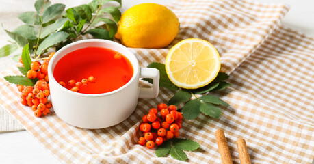 Cup of tasty rowan tea, berries and lemon on light background