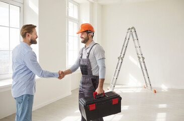 Professional construction worker and man client confirming agreement about house renovation or architectural project, shaking hands while posing in empty room, agree about future design