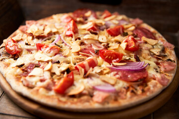 Pizza with ham, salami, cherry tomatoes and mozzarella cheese. Rustic wooden background. Soft focus. Close up.	