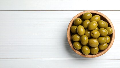 Elegant wooden bowl filled with vibrant green olives on textured white wood