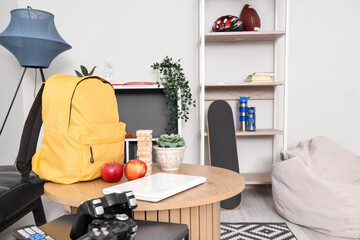 Yellow backpack with apples, laptop and game on table in children's room