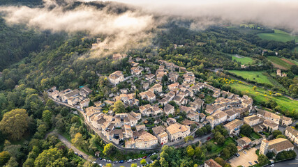 Aerial view of Mirmande village in France with morning fog over hills – picturesque medieval town surrounded by lush green forest and countryside landscape, historic architecture under soft misty sky