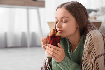 Beautiful young woman in warm sweater drinking hot mulled wine at home