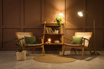 Comfortable armchairs, shelving unit and glowing lamps in interior of dark living room
