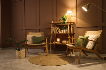Comfortable armchairs, shelving unit and glowing lamps in interior of dark living room