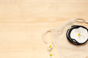 Bag, reusable cotton pads and chamomile flowers on wooden background, closeup