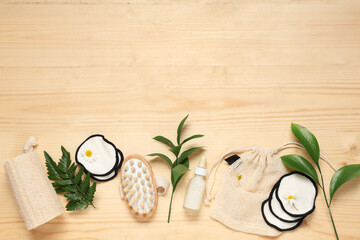 Composition with bag, reusable cotton pads, massage body brush and green twigs on wooden background
