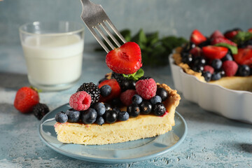 Plate with piece of delicious berry pie and fork with strawberry on blue grunge background, closeup