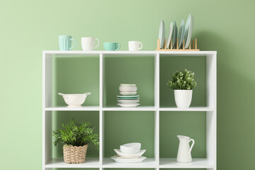 Shelf unit with clean dishware and houseplants in kitchen, closeup