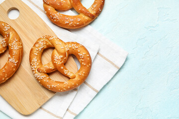 Cutting board with tasty pretzels on blue grunge background, closeup