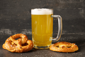 Glass of beer and tasty pretzels on black grunge background, closeup