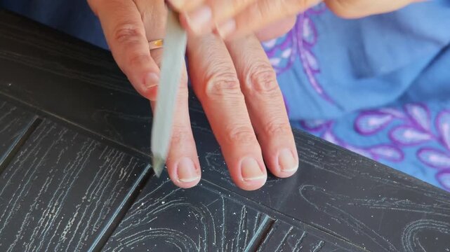 Refined female hands filing and shaping fingernails with professional nail file, focusing on precise nail care routine against dark wooden background