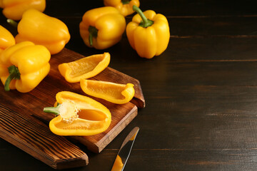 Cutting board with yellow bell peppers on wooden background, closeup
