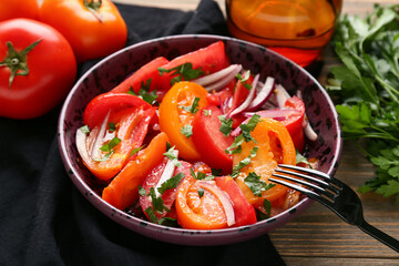Bowl of fresh tomato salad with red onion and parsley on wooden background, closeup
