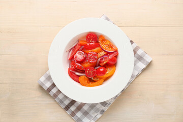 Plate of fresh tomato salad with red onion on beige wooden background