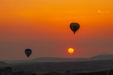 Hot air balloon flying over rocky landscape at sunrise in Cappadocia. Turkey