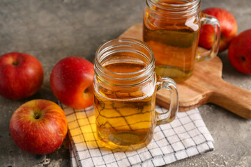 Mason jars of fresh apple cider and fruits on grey background, closeup