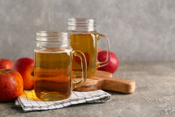 Mason jars of fresh apple cider and fruits on grey background