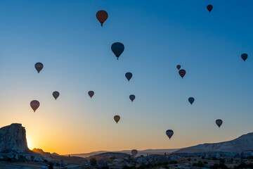Hot air balloon flying over rocky landscape at sunrise in Cappadocia. Turkey