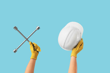 Male hands holding hardhat and cross wrench on blue background