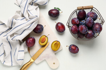 Basket and cutting board with fresh ripe plums on white background