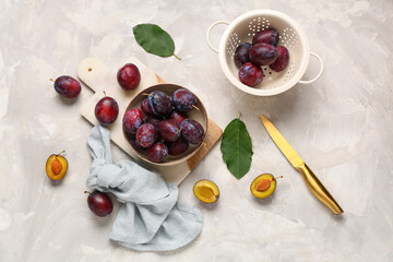 Bowl and colander with fresh ripe plums on grey background