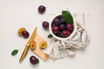 Colander and wooden board with fresh ripe plums on white background