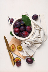 Colander and wooden board with fresh ripe plums on white background