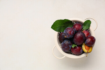 Colander with fresh ripe plums on white background