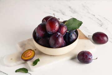 Bowl with fresh ripe plums on white background, closeup