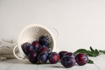 Colander with fresh ripe plums on white tile table