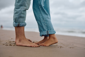 Romantic couple sharing a kiss on the beach, standing on tiptoe, capturing the essence of love with only their feet and legs visible
