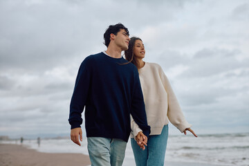 Romantic couple walking hand in hand along the beach on a cloudy day, enjoying each other’s company amidst the scenic ocean waves