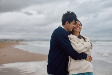 Romantic couple embracing on the beach, enjoying a quiet moment together despite the overcast sky