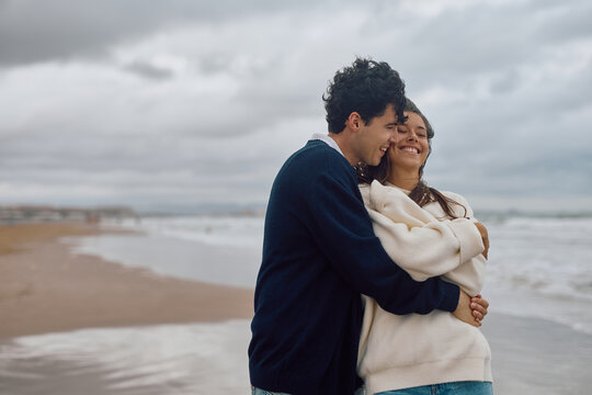 Romantic couple embracing on the beach, enjoying a quiet moment together despite the overcast sky - Powered by Adobe