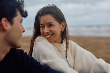 Obraz premium Happy young woman smiling at her boyfriend while spending time together on the beach on a cloudy day