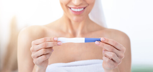 Expecting baby, great news and expression of happy emotions. Glad millennial pretty lady in towel looks at positive pregnancy test, on white bathroom background, close up, cropped, free space
