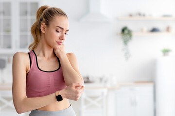 Woman in athletic suit feeling arm hurt after exercise at home. Danger of self-training. Young...