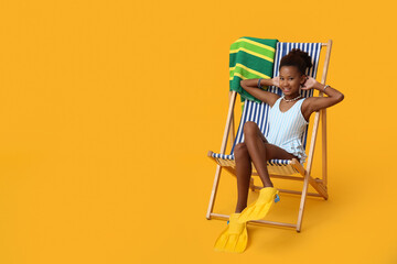 Cute little African-American girl in swimsuit and flippers sitting on deckchair against yellow background © Pixel-Shot