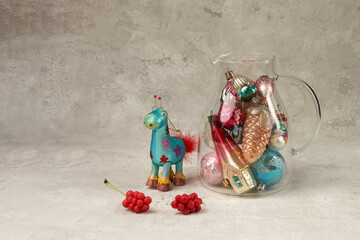 Glass jug filled with Christmas tree decorations and a Christmas tree decoration horse on a gray craquelure background. Copy space.
