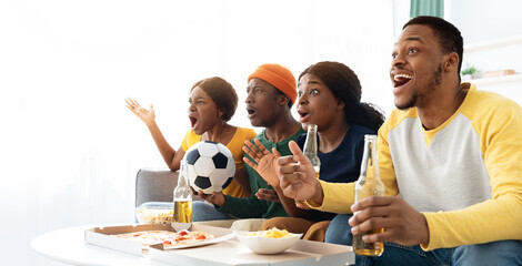 Emotional african american friends drinking beer and eating snacks, watching football game on TV at home, copy space. Cheerful black men and women fans watching sport match, gesturing and screaming © Prostock-studio