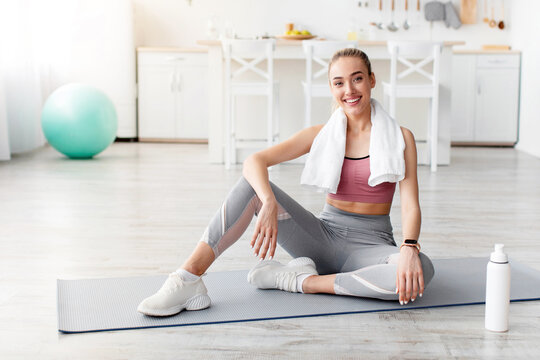 Satisfied european pretty young blonde fitness blogger resting after workout at home with water, woman take break on mat at domestic gym. Healthy lifestyle, body care, aqua balance and remote lesson